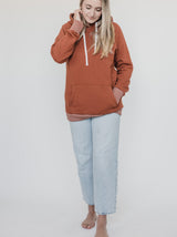 Blonde woman wearing the Blondie Classic Forest Hoodie in Gingerbread Red with heather cuffs and hem