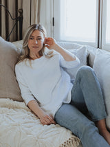 blonde woman sitting on a sofa wearing a classic east end sweater in white