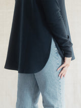 A person wearing a dark navy long-sleeve Blondie Classic Dusk Sweater and light blue jeans, shown from the chest down against a light neutral wall.