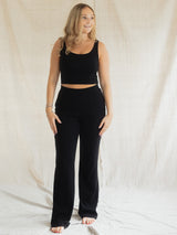 A woman modeling a black two-piece lounge set consisting of a cropped tank top and high-waisted Blondie Juniper pant, standing against a draped off-white fabric backdrop.