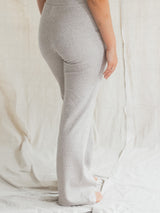 A person wearing light heather Flax gray Blondie Juniper pant, shown from the waist down against a draped off-white fabric backdrop.