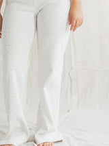 A close-up of a person wearing white Confetti textured Blondie Juniper pant, standing barefoot against a white fabric backdrop.