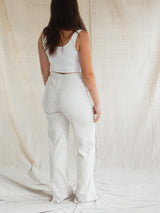 A woman shown from behind wearing a matching white two-piece loungewear set consisting of a cropped tank top and white Confetti textured Blondie Juniper pant, posed against a draped beige fabric backdrop.