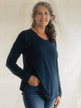 A smiling woman with gray hair wearing a dark navy blue Blondie Long-Sleeve Janis T-shirt and blue jeans, standing against a neutral textured beige backdrop.