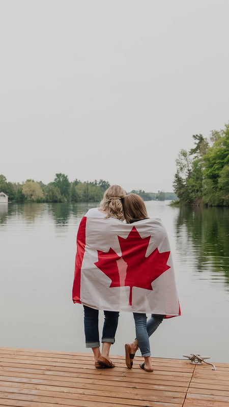 Blondie apparel founders wrapped in the Canadian flag looking onto a beautiful lake
