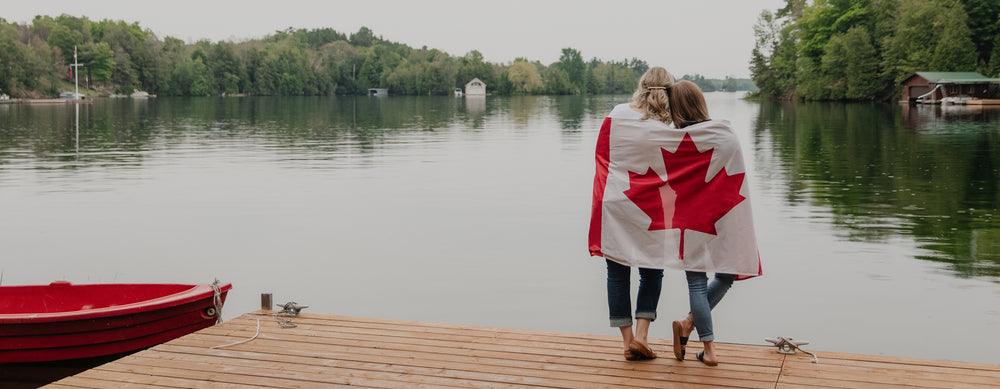 Blondie apparel founders wrapped in the Canadian flag looking onto a beautiful lake
