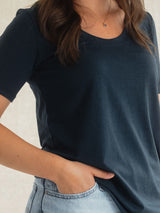 A close-up of a person wearing a dark navy blue short-sleeve Blondie New Rideau Shoreline t-shirt and light-wash blue jeans, with one hand in the pocket.